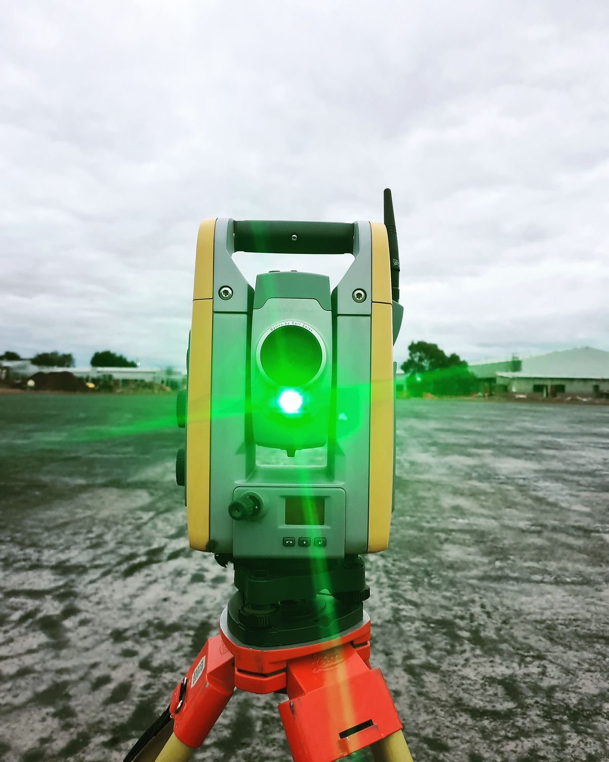 Estação total sobre tripé num terreno em obras, com a luz-guia verde acesa